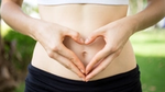 A woman making a heart shape with her hands in front of her gut.