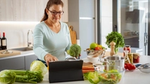 Woman in kitchen using tablet with fresh vegetables around.
