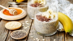 Two cups with chia seed puddings, next to a banana, chia seeds and honey.